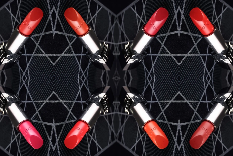 Symmetrical close-up of lipstick tubes in various red shades with silver casings, arranged on a black geometric-patterned backdrop.
