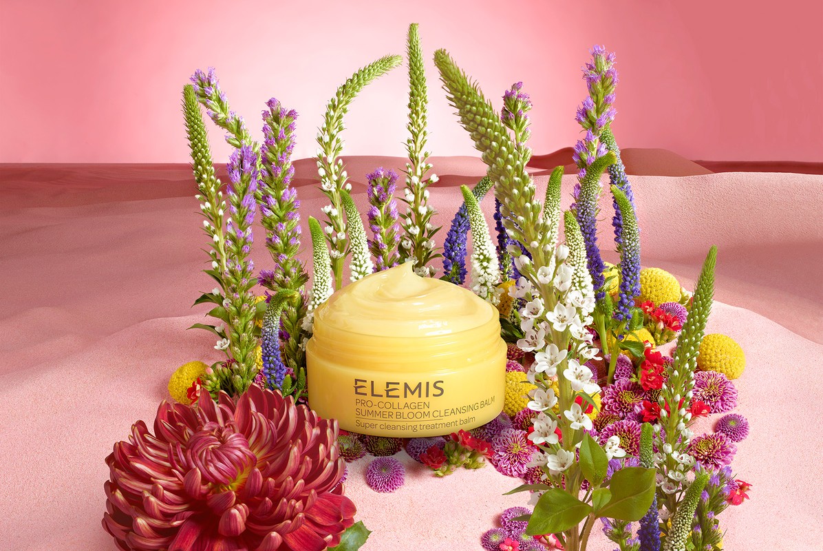 Yellow cleansing balm surrounded by colorful spring blossoms, pink backdrop. Beauty product shot for skincare or floral design concept.