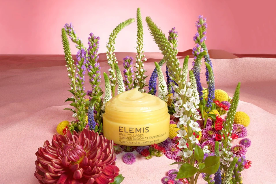 Yellow cleansing balm surrounded by colorful spring blossoms, pink backdrop. Beauty product shot for skincare or floral design concept.