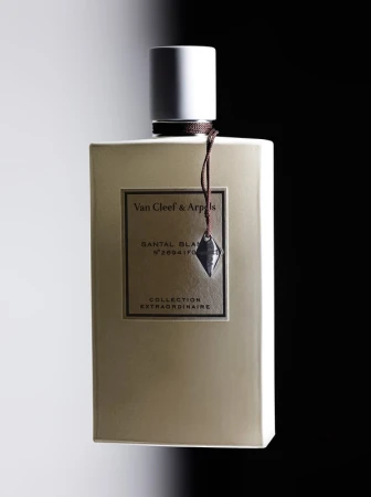 Rectangular Van Cleef & Arpels perfume bottle with a white cap and tan body on a split black and white background, studio lit.