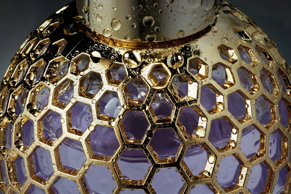 Close-up of a gold perfume bottle with a purple liquid interior and water droplets on its surface, showcasing luxury and detail.