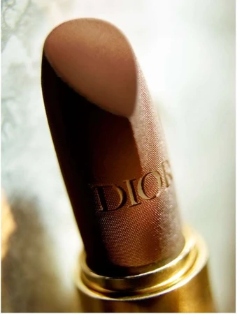 Close-up of a Dior lipstick with embossed lettering in a metallic gold case against a soft textured background.