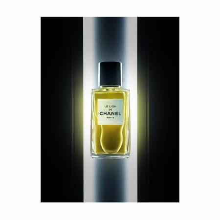 A rectangular glass perfume bottle with a black cap centered against a vertical illuminated column and dark background.