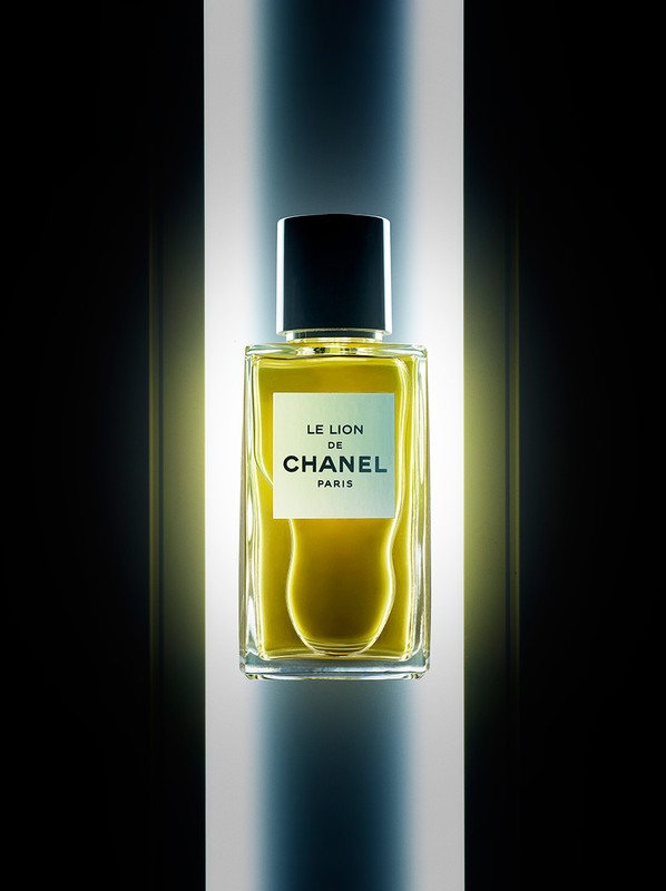 Close-up studio shot of a clear glass perfume bottle with amber liquid and black cap, featuring Chanel logo, on a softly lit background.