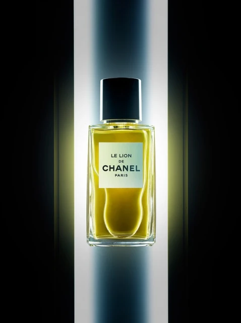 Close-up studio shot of a clear glass perfume bottle with amber liquid and black cap, featuring Chanel logo, on a softly lit background.
