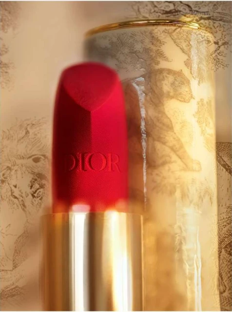 Close-up of red Dior lipstick with a gold base, beside a patterned canister featuring sketched animals. Beauty and cosmetics product shot.