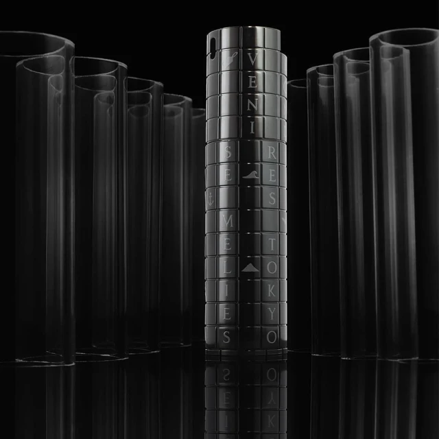 Close-up of a glossy black cylinder with text and geometric patterns, surrounded by clear tubes against a stark black backdrop.
