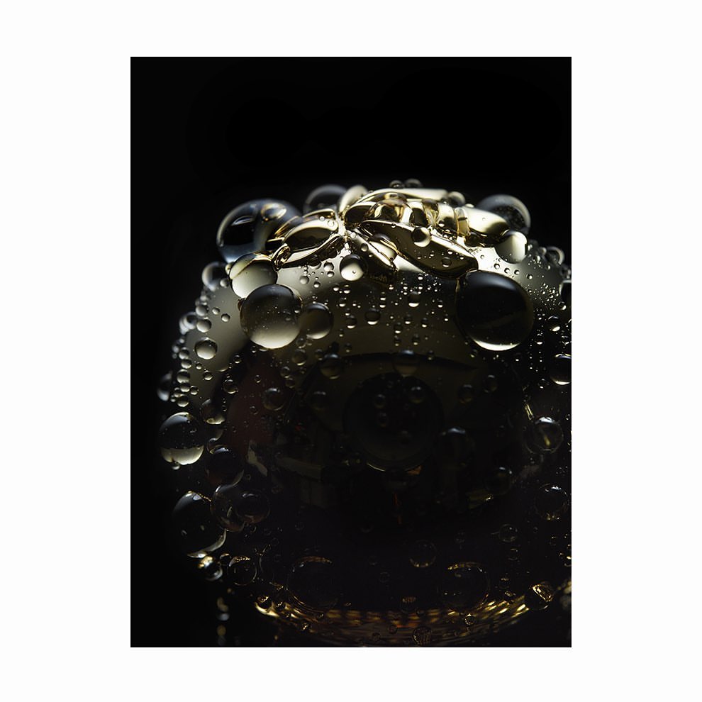 Close-up macro shot of a gold metallic spherical object covered in water droplets against a dark background.