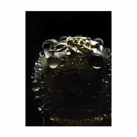Close-up macro shot of a gold metallic spherical object covered in water droplets against a dark background.