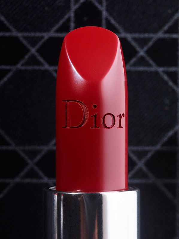Close-up of red Dior lipstick with a silver tube against a black patterned background, capturing luxury beauty and cosmetics.