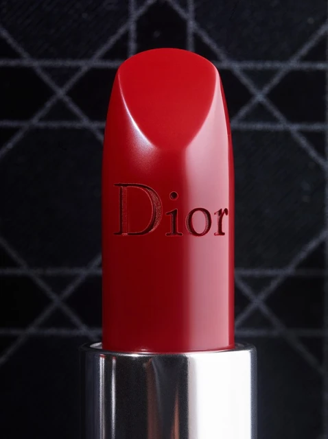 Close-up of red Dior lipstick with a silver tube against a black patterned background, capturing luxury beauty and cosmetics.