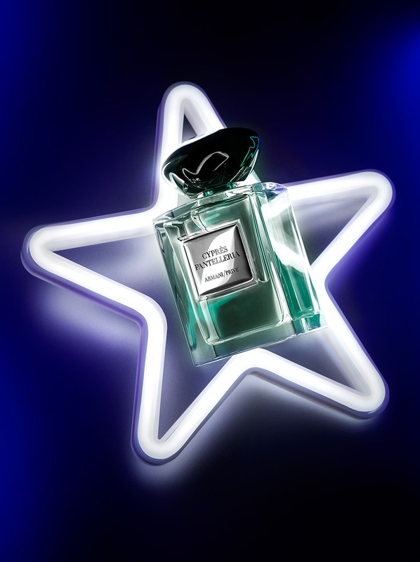 Elegant fragrance bottle by Armani Prive, Cyprus Pantelleria, highlighted with soft neon star glow on a graduated blue backdrop. 