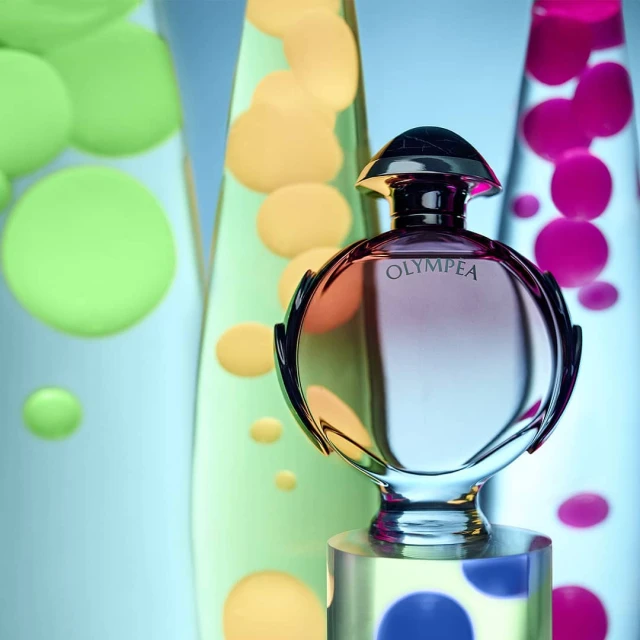 Shiny perfume bottle on a polka-dot cube stand in front of lava lamps with green, orange, and pink liquid bubbles.