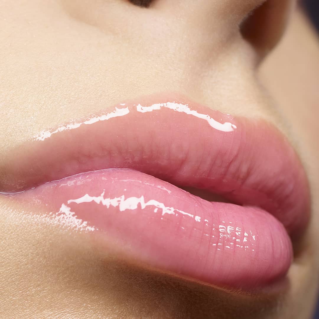 Close-up of an adult female's shiny lips covered in pink lip gloss and framed by light skin, emphasizing a beauty or makeup concept.