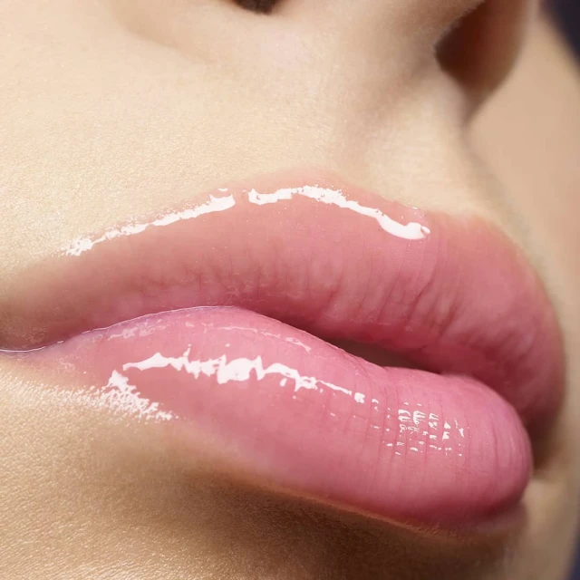 Close-up of an adult female's shiny lips covered in pink lip gloss and framed by light skin, emphasizing a beauty or makeup concept.