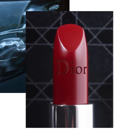 Close-up product shot of a red lipstick with the Dior logo embossed on the side against a dark patterned background.