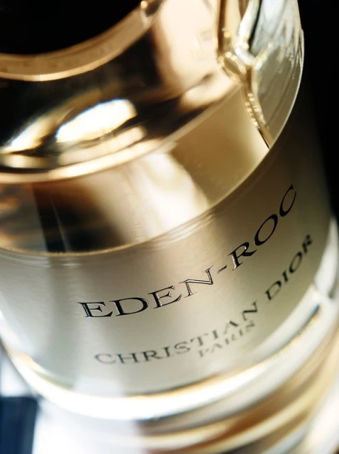 Close-up studio shot of a light gold Christian Dior Eden-Roc perfume bottle featuring black sans-serif text on the label.