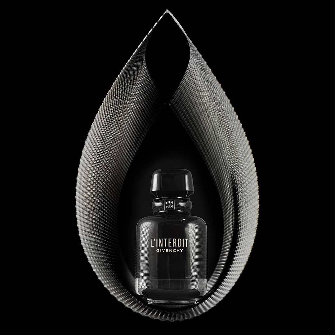 Elegant studio shot of a 'L'Interdit Givenchy' perfume bottle encased by a teardrop-shaped, metallic fabric structure on a black backdrop.