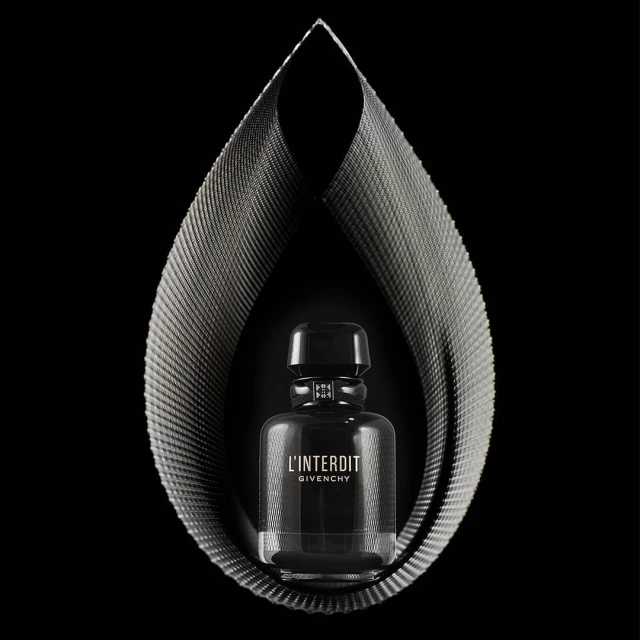 Elegant studio shot of a 'L'Interdit Givenchy' perfume bottle encased by a teardrop-shaped, metallic fabric structure on a black backdrop.