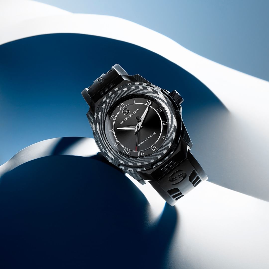 Studio shot of a black automatic wristwatch on a blue and white abstract background, showcasing its design and details.