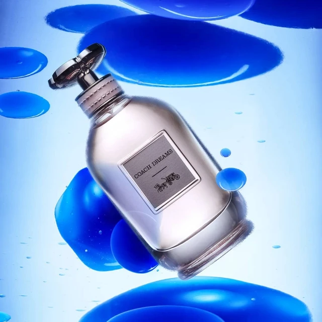 Coach Dreams perfume bottle floats in the air surrounded by floating cobalt liquid spheres, product shot, studio lighting.