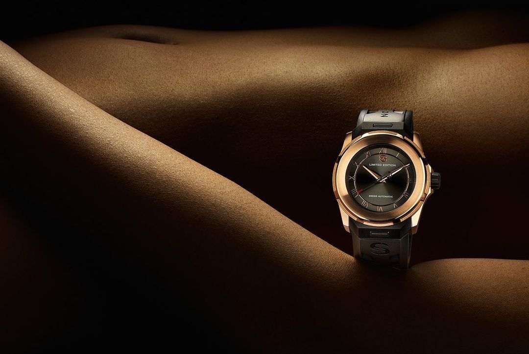 Close-up of a gold and black wristwatch on a tan surface with subtle contours and shadows, creating a luxurious and minimalist aesthetic.