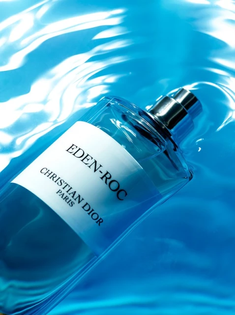 Glass bottle of Eden-Roc Christian Dior perfume in water with light reflecting off the surface. The bottle has a white label.