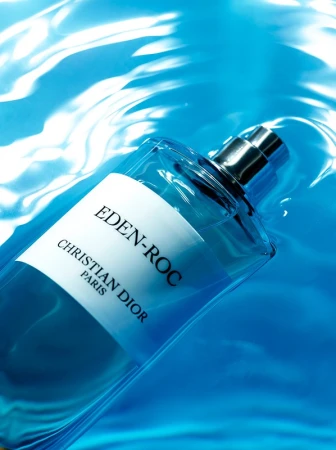 Glass bottle of Eden-Roc Christian Dior perfume in water with light reflecting off the surface. The bottle has a white label.