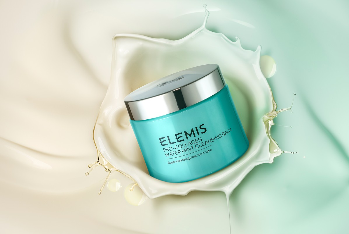 Turquoise jar of Elemis Pro-Collagen Water Mint Cleansing Balm surrounded by a swirl of white cream against a gradient backdrop.