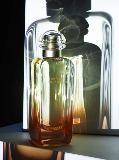 Elegant rectangular perfume bottle with clear cap, filled with a gradient of golden liquid, and the Hermes logo, stands in a studio setting.