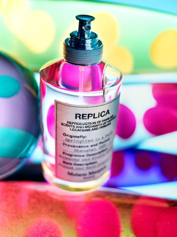 Close-up of a transparent perfume bottle with a pink liquid against a background featuring colorful bokeh effects and polka dots.