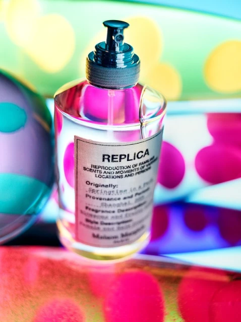 Close-up of a transparent perfume bottle with a pink liquid against a background featuring colorful bokeh effects and polka dots.