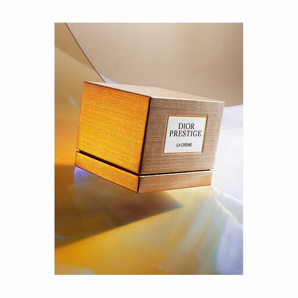 Elevated shot of Dior Prestige La Crème box with light brown and gold texture, displayed against a shimmering gold reflective surface.