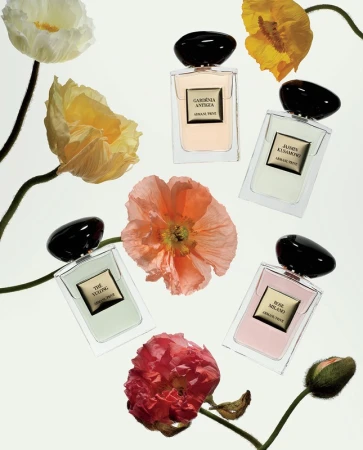 Five perfume bottles are arranged among pink, orange, yellow and white poppies with green stems against a bright white background.