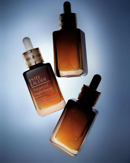 Three Estee Lauder Advanced Night Repair serum bottles arranged at angles against a graduated blue background with soft lighting.
