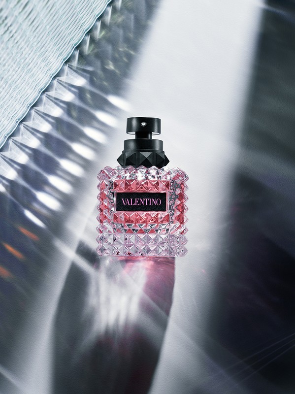Valentino perfume bottle close-up on a reflective surface with light patterns. Beauty and fashion product, studio shot. 