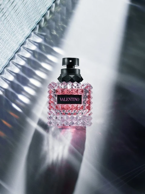 Valentino perfume bottle close-up on a reflective surface with light patterns. Beauty and fashion product, studio shot. 