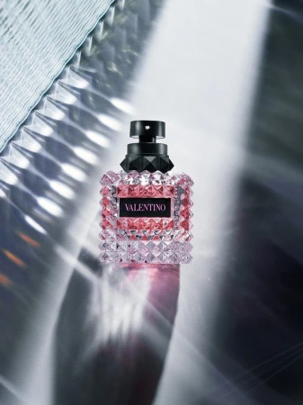Valentino perfume bottle close-up on a reflective surface with light patterns. Beauty and fashion product, studio shot. 
