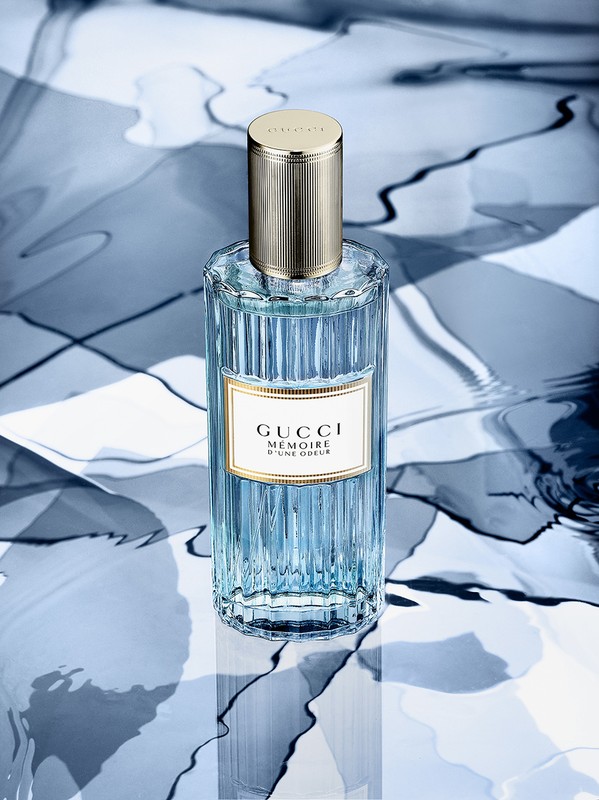 Gucci Mémoire d’une Odeur perfume bottle on a surface with an abstract blue and white pattern, showcasing its design.