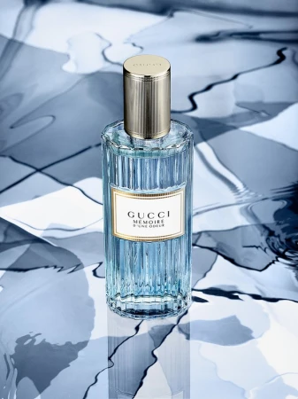 Gucci Mémoire d’une Odeur perfume bottle on a surface with an abstract blue and white pattern, showcasing its design.