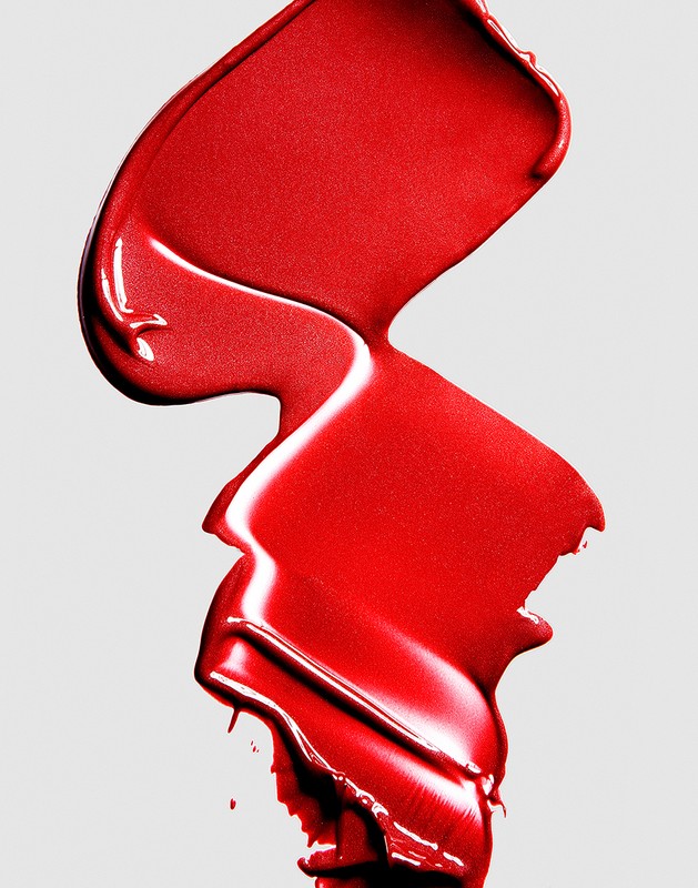 Close-up of a vibrant red lipstick smear against a neutral background, showcasing rich texture and intense pigmentation for beauty concepts.