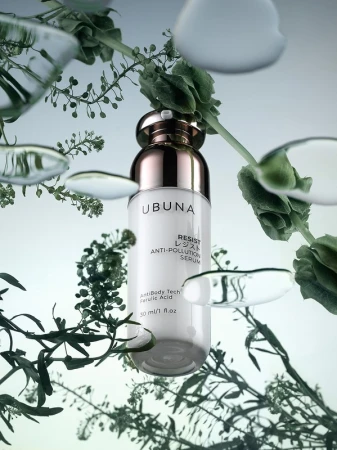 Cosmetic serum bottle by Ubuna in studio product shot with botanical sprigs and water droplets, white bottle with gold accents.