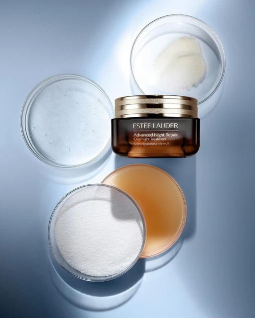 Estee Lauder Advanced Night Repair cream jar with clear petri dishes on a blue surface in a beauty studio shot, product focus.