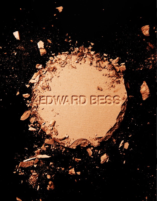 Top-down studio shot of shattered tan-colored face powder by Edward Bess on black backdrop. Beauty product for cosmetics brand.