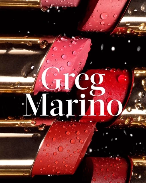 Close-up of staggered lipsticks with gold tubes in red and pink tones, with water droplets against a dark background. 