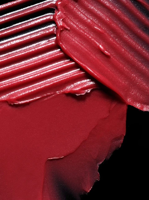 Textured smears of deep red lipstick or cosmetic product against a black background, showcasing color and product consistency.