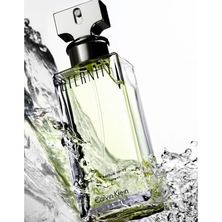 Close-up of a Calvin Klein Eternity perfume bottle with silver accents, surrounded by splashing water against a white background.