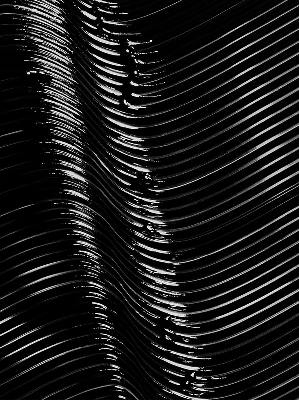 Abstract high-angle close-up photograph of shiny parallel ridges creating a textured monochrome pattern with smooth highlights and shadows.