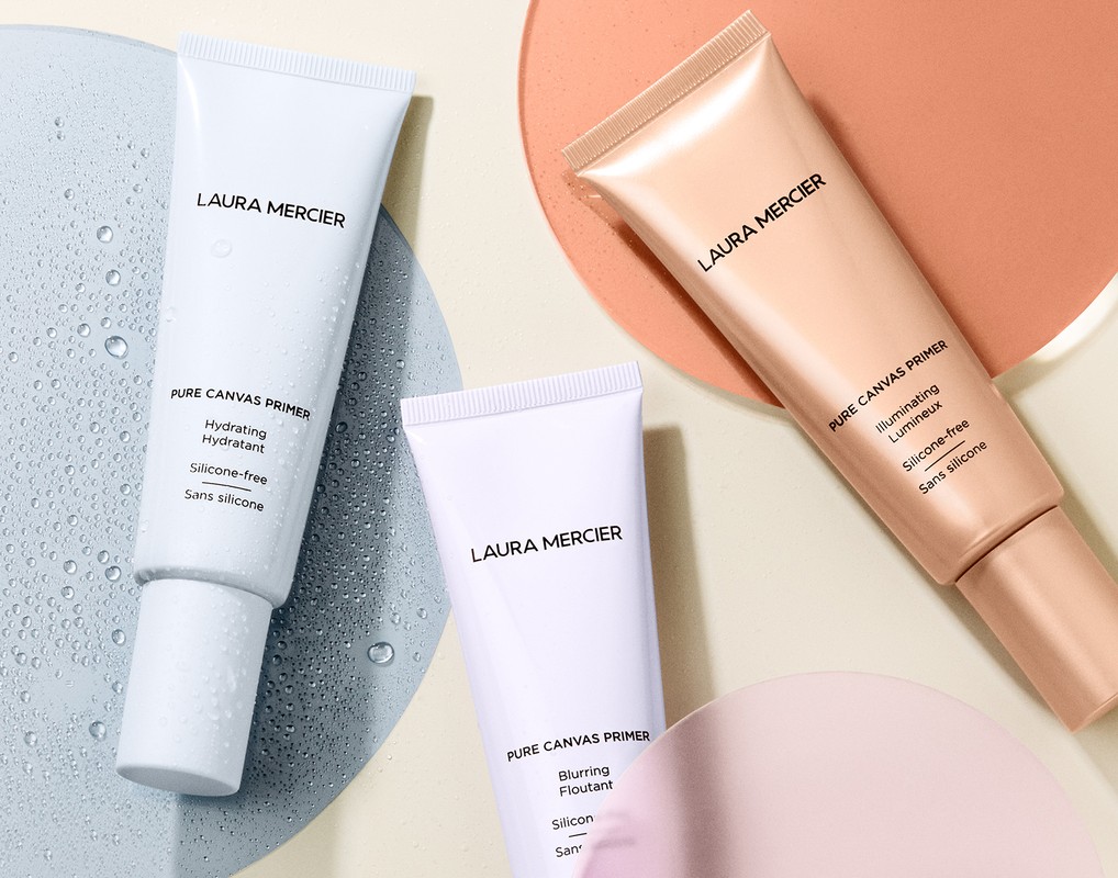 Close-up of Laura Mercier Pure Canvas Primers in hydrating, illuminating, and blurring formulas, with water droplets on surface, beauty product.