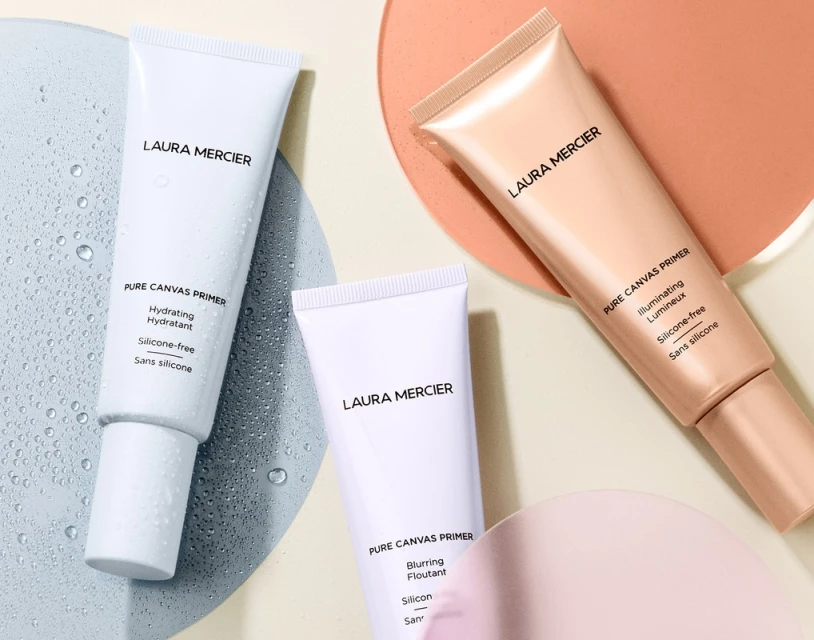Close-up of Laura Mercier Pure Canvas Primers in hydrating, illuminating, and blurring formulas, with water droplets on surface, beauty product.